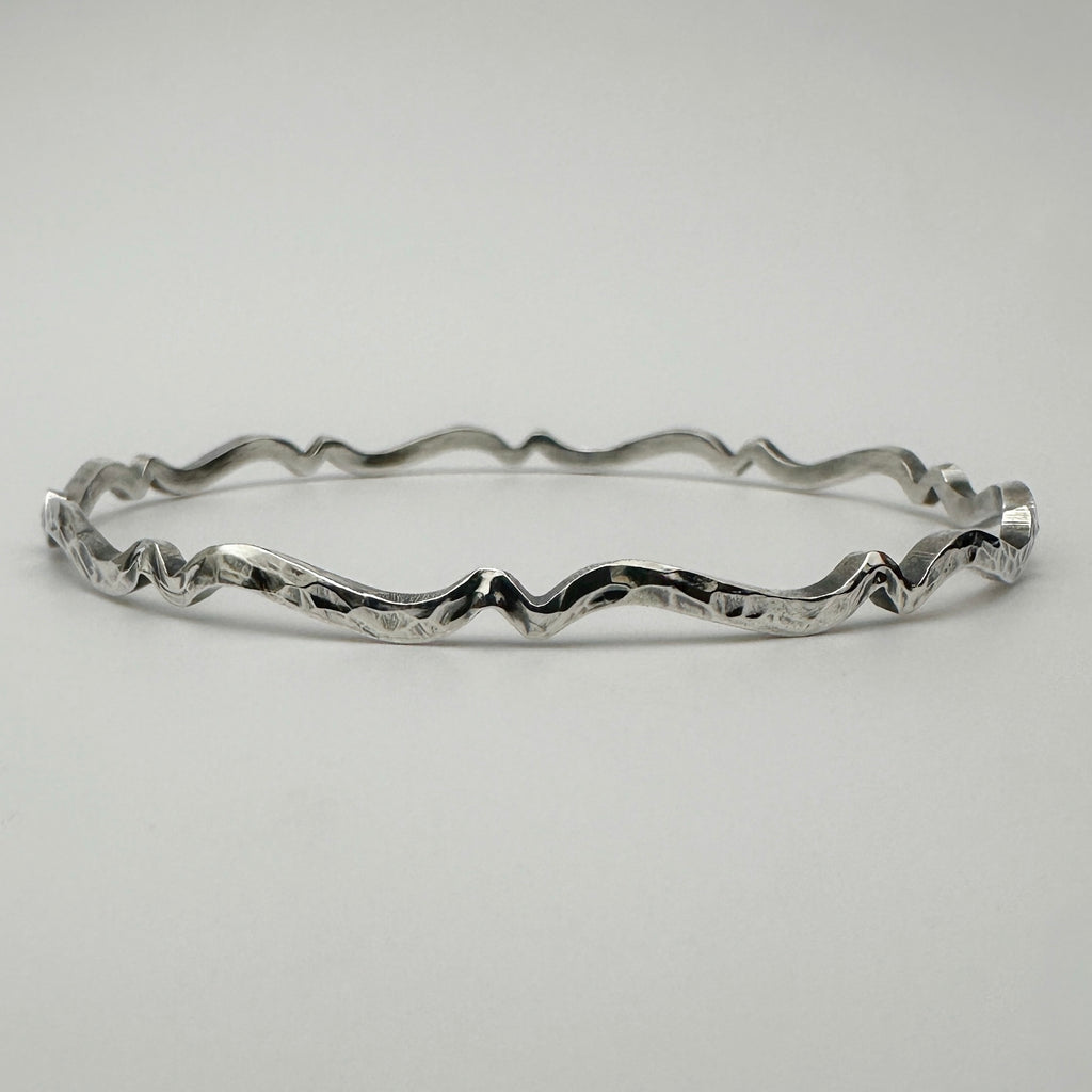 Bespoke silver bracelet with wavy oxidised and textured design on a light gray background handmade in Nottingham