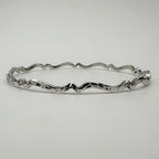 Bespoke silver bracelet with wavy oxidised and textured design on a light gray background handmade in Nottingham