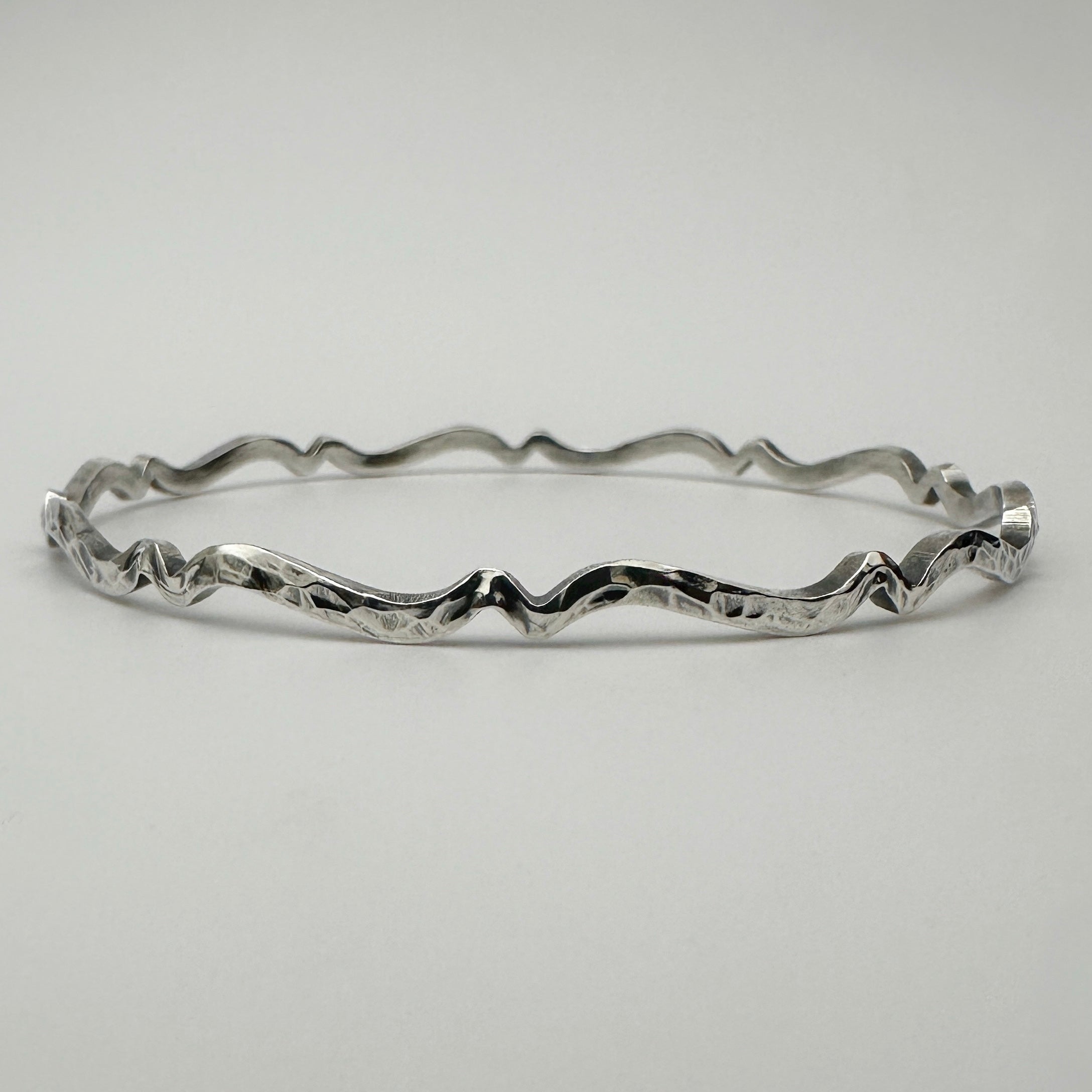 Bespoke silver bracelet with wavy oxidised and textured design on a light gray background handmade in Nottingham