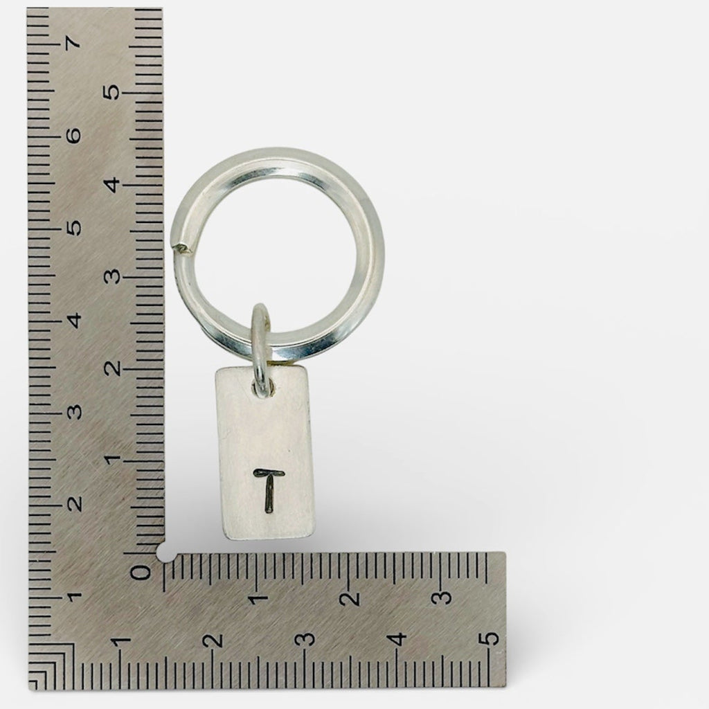 Handmade sterling silver keyring against a ruler with hand stamped initials T  made by a small independant jeweller in Nottingham