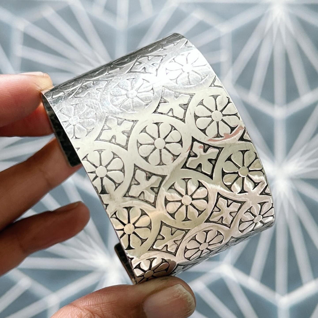 Wide sterling silver jewellery cuff made in Nottingham by Bottlebee on a geometric blue background held in a hand