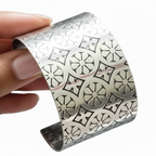 Silver bracelet with intricate art deco pattern held by a hand on a white background made in Nottingham sustainably by Bottlebee