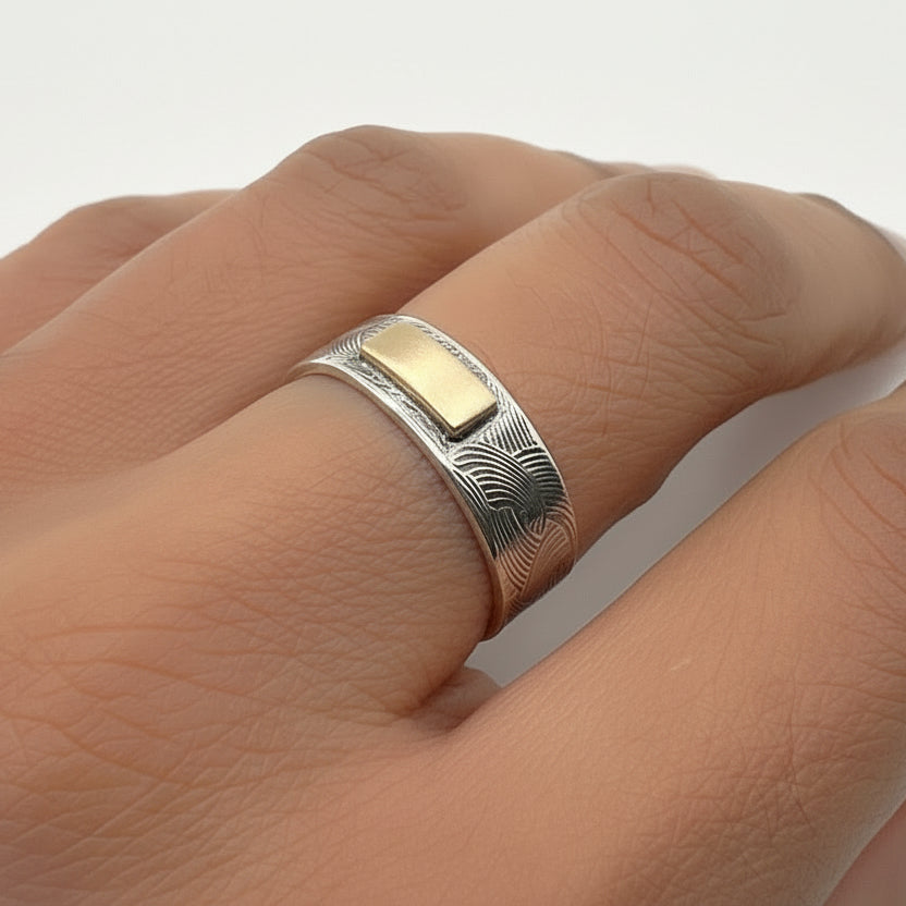Solid silver ring with a gold centre bar on a person's finger against a white background