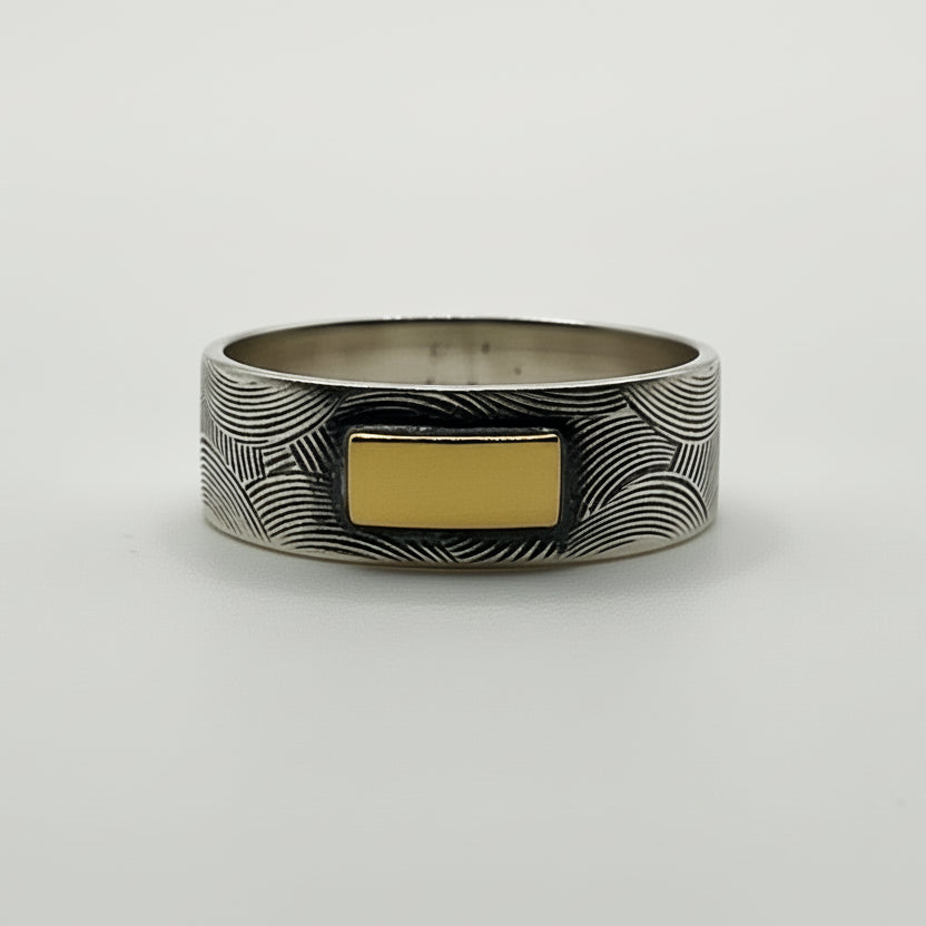 Sterling silver patterned and oxidised ring with a gold accent on a white background