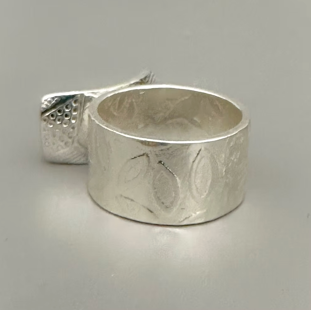 Silver ring with textured design on a gray background