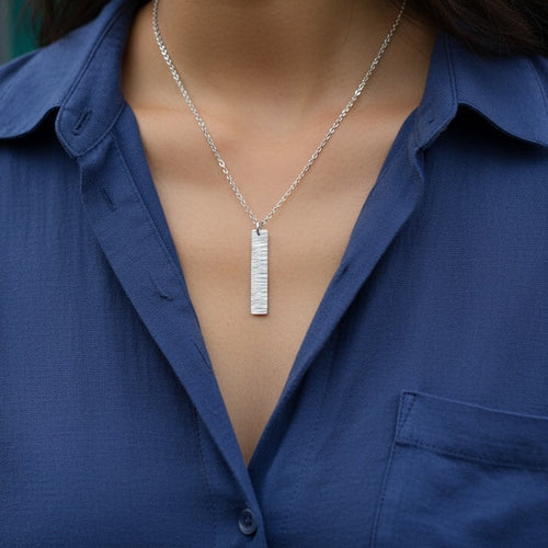Woman wearing a blue shirt with a bespoke 925 silver necklace jewellery made in Nottingham against a blue tiled wall.