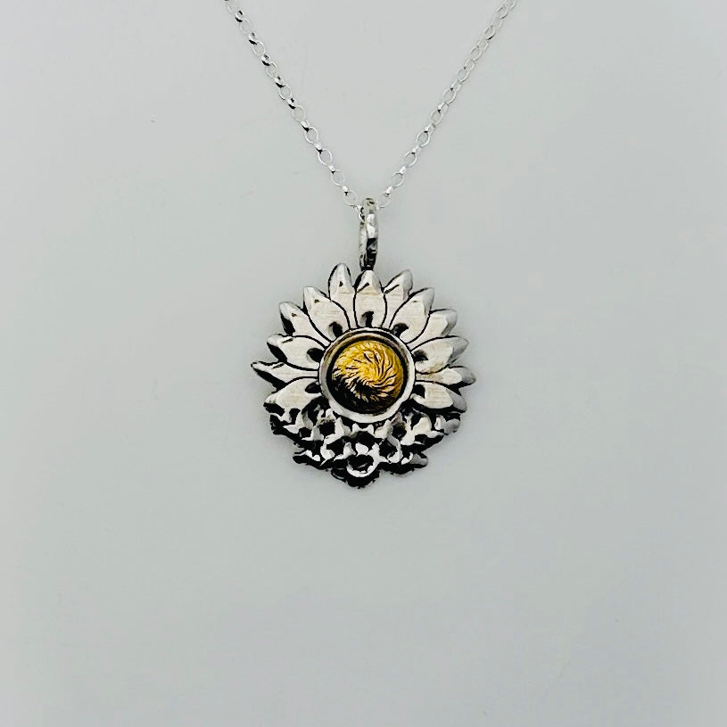 silver and gold necklace with a sunflower and butterfly shaped pendant on a white background. The butterflies are merging with the sunflower and the head of the sunflower in the middle of the pendant is made from 18ct gold. Handmade jewellery in Nottingham