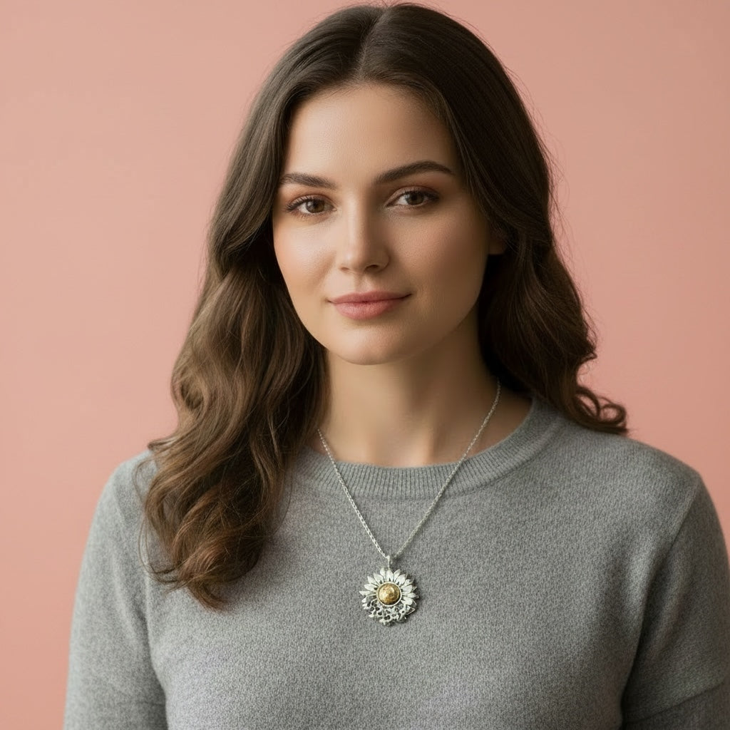 woman wearing a grey top in front of a pink bacgrround wearing a sterling silver and 18ct gold necklace with a sunflower and butterfly shaped pendant on a white background. The butterflies are merging with the sunflower and the head of the sunflower in the middle of the pendant is made from 18ct gold. Handmade jewellery in Nottingham