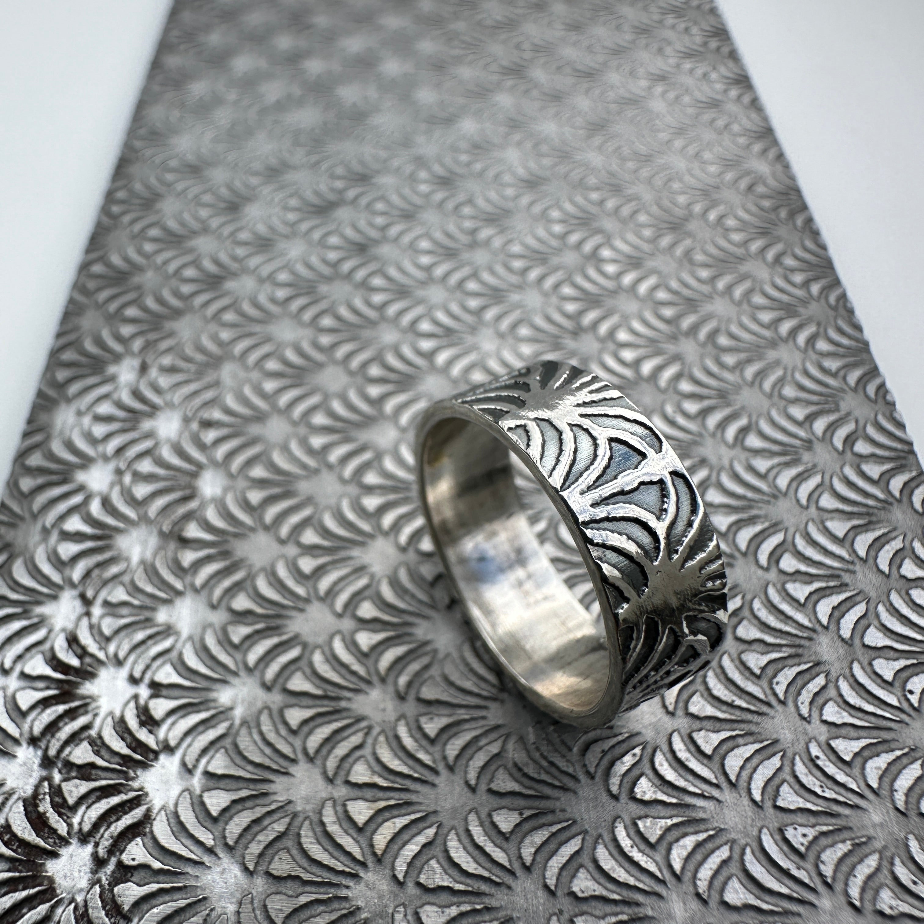 unique art deco jewellery silver wedding ring band for a man or woman or unisex resting on a pattern plate on a light grey background handmade sustainable bespoke jewellery Nottingham