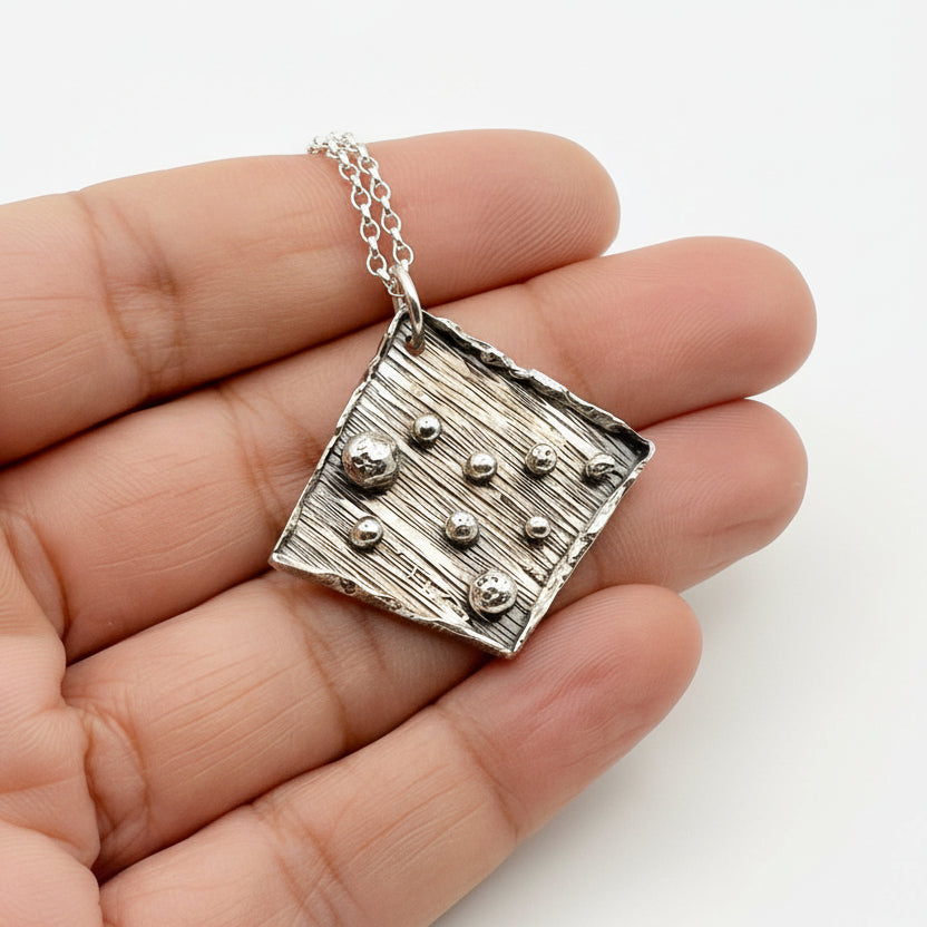 Bespoke handmade 925 silver pendant held in a hand against a white background