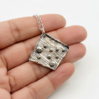 Bespoke handmade 925 silver pendant held in a hand against a white background