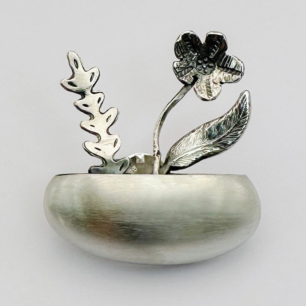 Sterling silver brooch with 3 floral designs on a light background