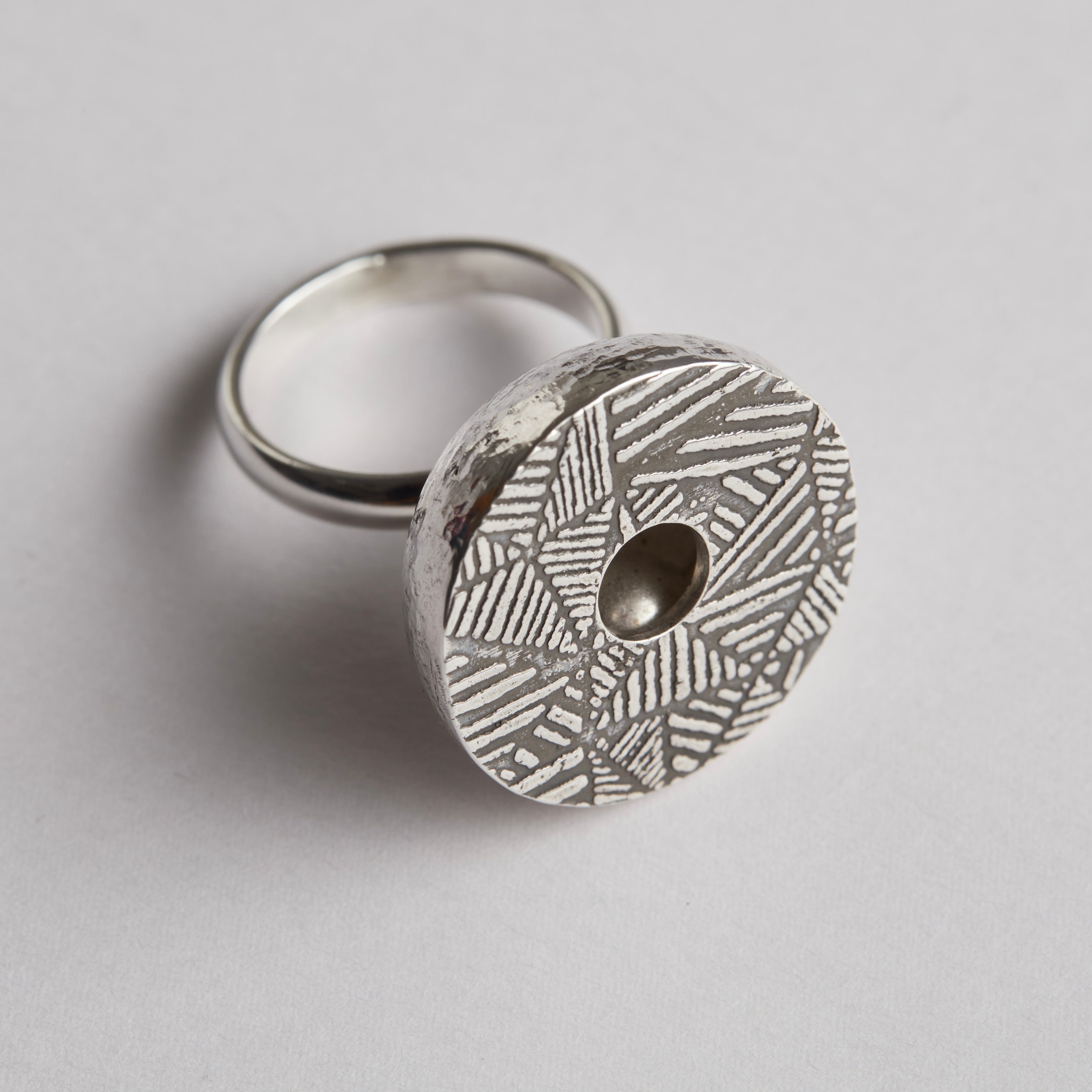 A sterling silver kinetic ring with a patterned and oxidised top with a hole in it which reveals a silver ball which moves