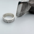 lined unique silver wedding ring band for a man or woman or unisex with textured surface next to a metal hammer on a light grey background handmade sustainable bespoke jewellery nottingham