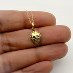 Gold skull pendant necklace held between fingers on a white background