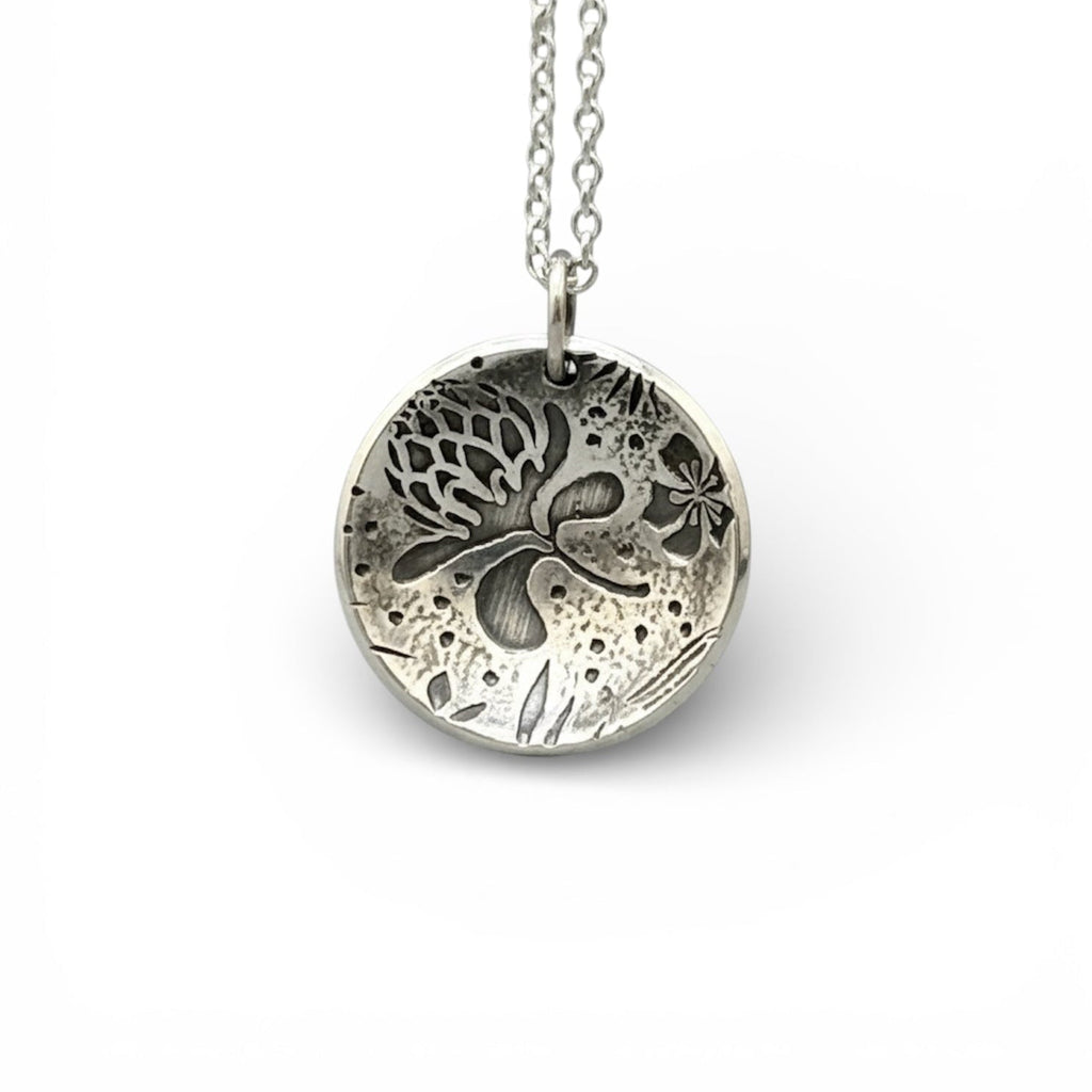 Silver necklace with a round pendant with thistles and flowers on a white background, handmade jewellery made by Bottlebee in Nottingham