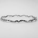Handmade sterling silver bangle with wavy design on a light grey background